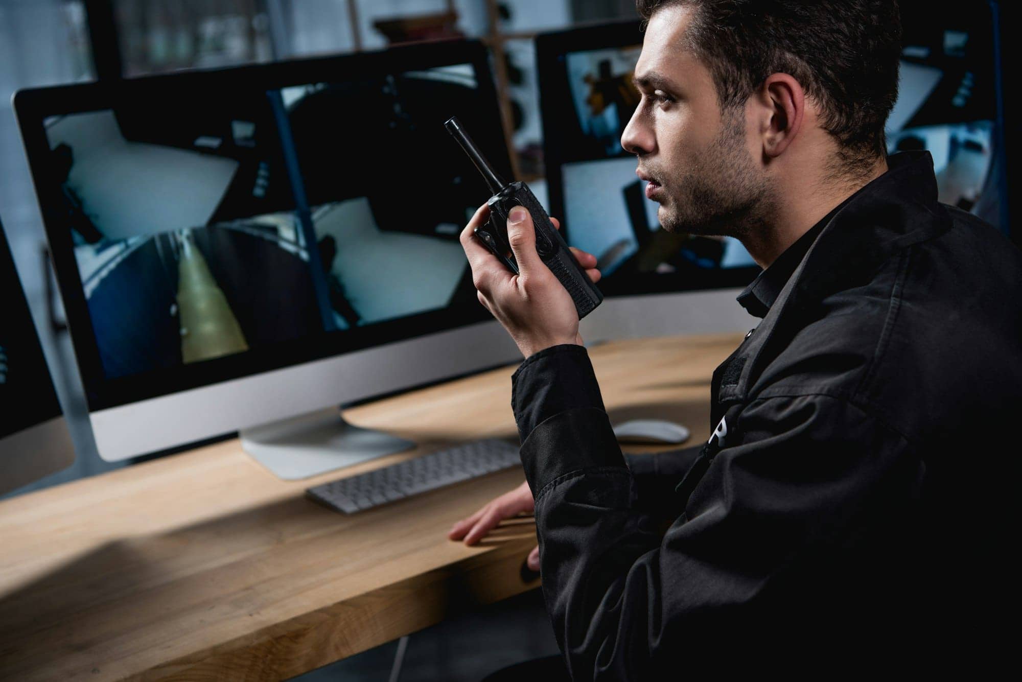 handsome guard in uniform holding walkie-talkie and looking at computer monitor